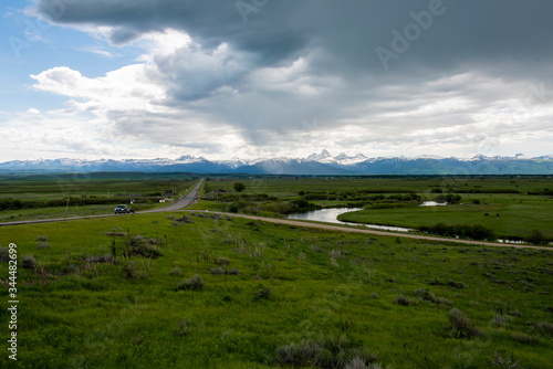 A view of the Teton mountains from several miles north of Victor, Idaho, with green agricultural fields and interesting clouds overhead
