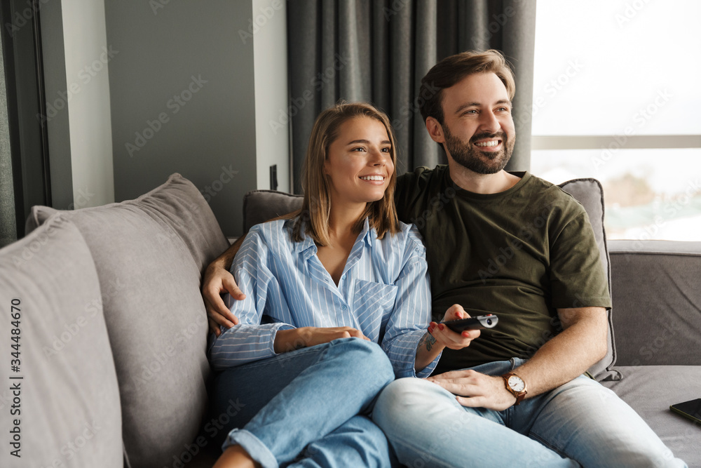 Photo of joyful couple watching TV and using remote control Photo of joyful couple watching TV and using remote control