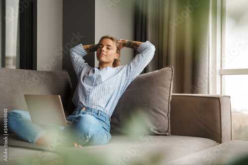 Image of young relaxed woman resting while sitting with laptop