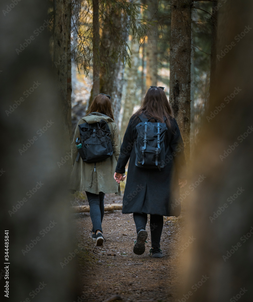 Teenage girls hiking through forest with hipster backpacks. Warm tones, sunset colors. Wilderness. Teenage girls hiking through forest with hipster backpacks. Warm tones, sunset colors. Wilderness.