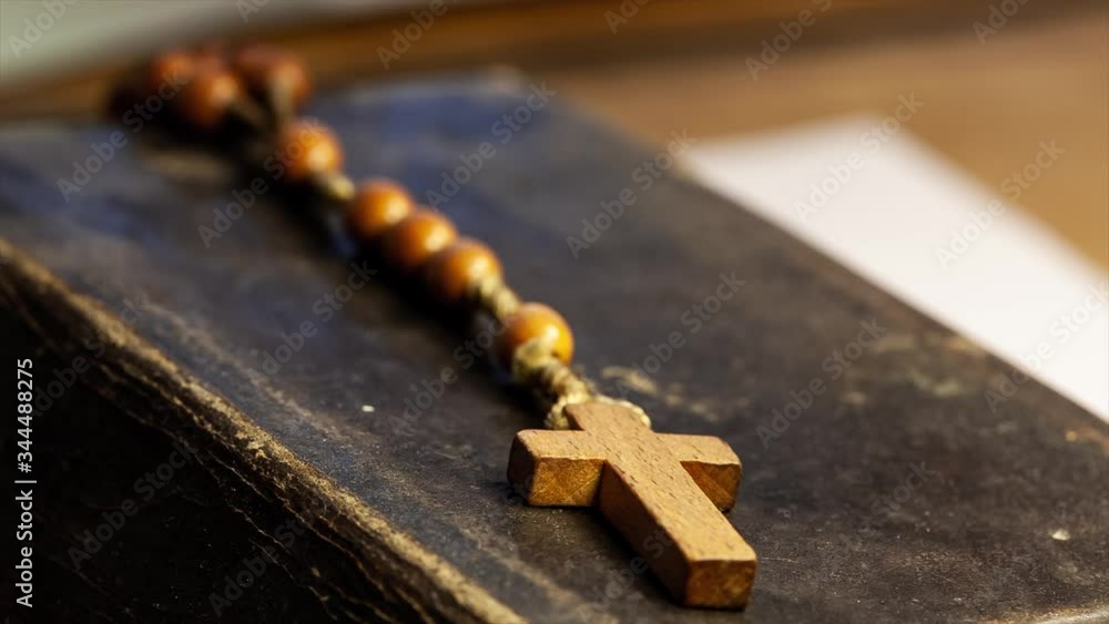 Small wooden rosary on an old dated prayer book rack to the cross focus macro, closeup. Religion - christianity, prayer and belief simple abstract concept, nobody. Objects, accessories. Focus shift Small wooden rosary on an old dated prayer book rack to the cross focus macro, closeup. Religion - christianity, prayer and belief simple abstract concept, nobody. Objects, accessories. Focus shift