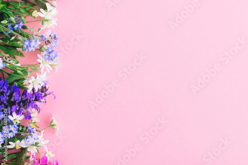 Wildflowers colorful border on pink paper background, flat lay with space for text. Blooming spring flowers, floral greeting card template. Happy Mother's day concept. Hello spring