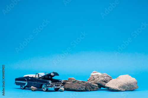 A car with its hood open next to a bunch of stones, on blue background.