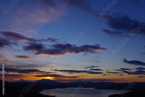 Fototapeta Naklejka Na Ścianę i Meble -  峰から望む夜明けの空のグラデーション。朝の太陽に照らされた雲。眼下の湖。北海道、日本。