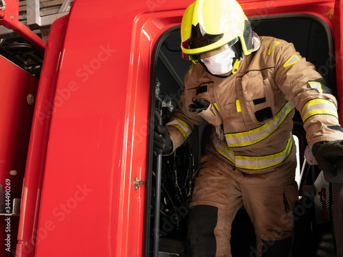 Firefighter getting down from the truck equipped with an intervention suit, helmet and mask to protect himself from the covid 19
