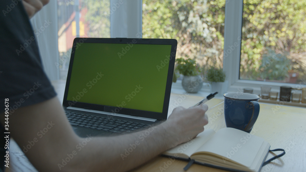 Working from home using a green screened laptop on the kitchen table with pens and a pad Working from home using a green screened laptop on the kitchen table with pens and a pad