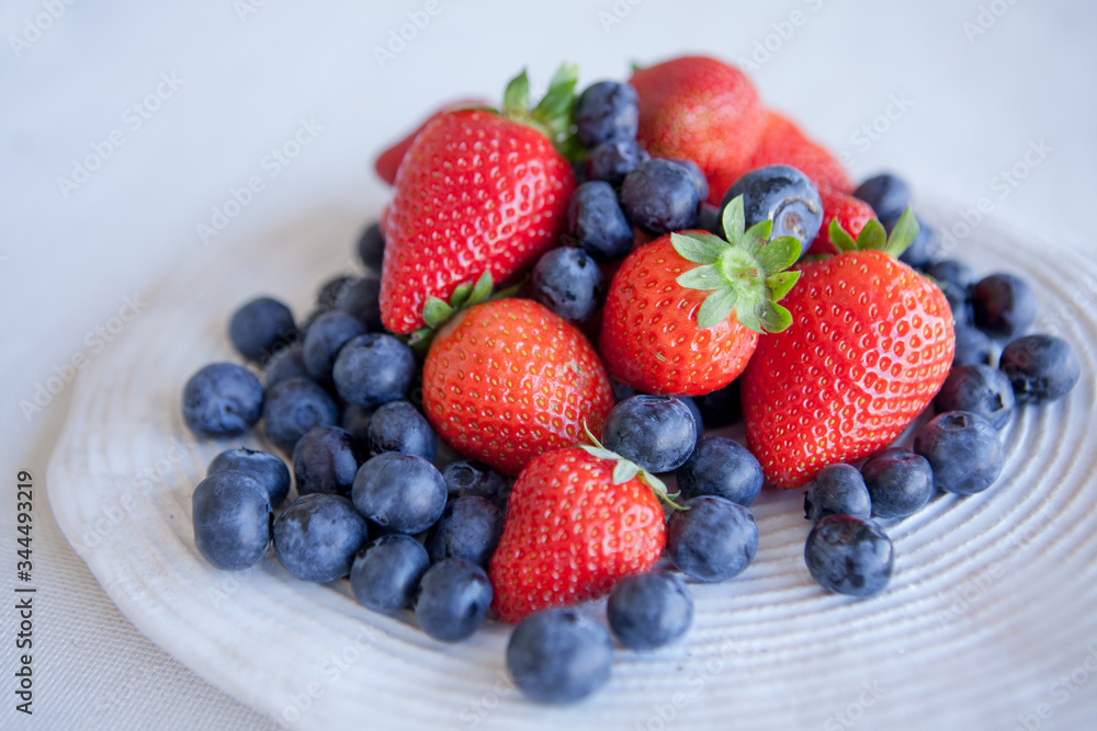 Blueberries and strawberries in a ceramic plate on the table. Natural light. Blueberries and strawberries in a ceramic plate on the table. Natural light.