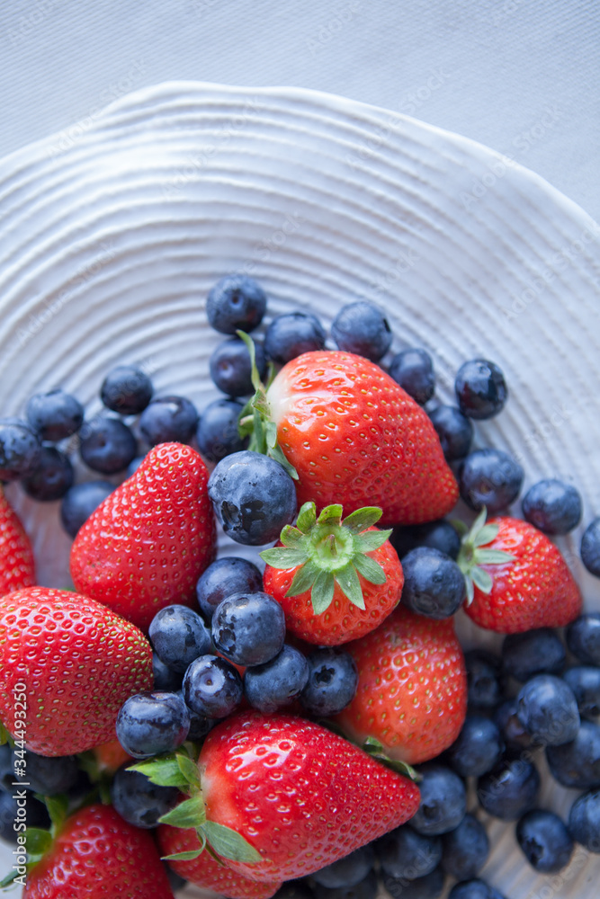 Blueberries and strawberries in a ceramic plate on the table. Natural light. Top view Blueberries and strawberries in a ceramic plate on the table. Natural light. Top view