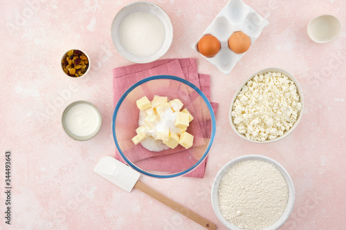 flour, cottage cheese in bowl and milk, eggs. products for making cheesecakes on a pink backround.
