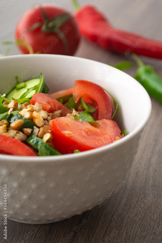 Healthy fresh summer salad with cucumbers, tomatoes, fresh arugula, chopped walnuts, pepper, olive oil and lemon juice on a rustic wooden surface Healthy fresh summer salad with cucumbers, tomatoes, fresh arugula, chopped walnuts, pepper, olive oil and lemon juice on a rustic wooden surface