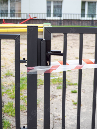 closed entrance to the Playground with a white and red fencing tape .metal gate . restriction during an epidemic