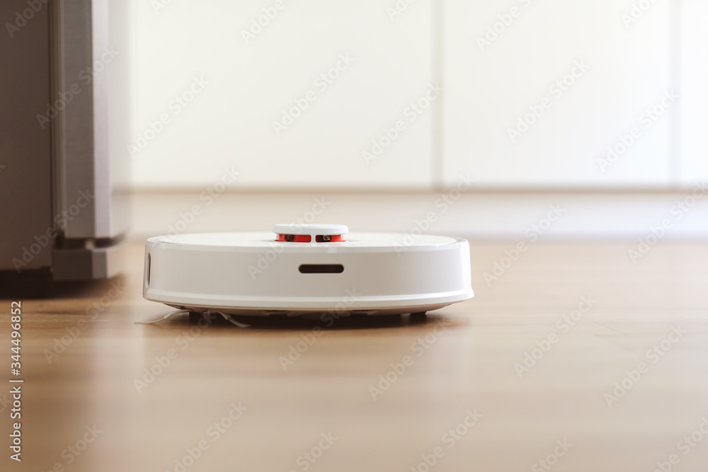 white robot vacuum cleaner cleans the floor from debris,home cleaning with an electric vacuum cleaner,vacuum cleaner electric robot cleaning technology,top view of a robot vacuum cleaner. white robot vacuum cleaner cleans the floor from debris,home cleaning with an electric vacuum cleaner,vacuum cleaner electric robot cleaning technology,top view of a robot vacuum cleaner.