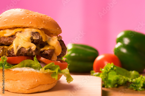 Classic beef burger with double patty, cheese, lettuce, onion, tomato on green capsicum Background