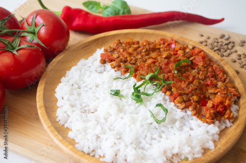 Red lentil ragu dahl with tomatoes, pepper, greens and rice on a wooden plate