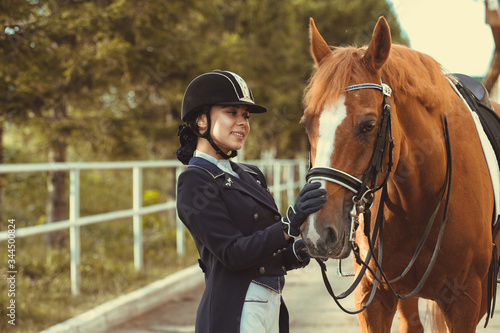 Beautiful professional female jockey standing near horse. woman horse rider is preparing to equitation. girl and horse. equestrian sport concept. dressage horse  © matilda553