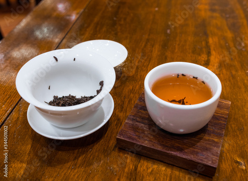 Gong Fu Cha brewing. Beautiful white porcelain (Gaibei/ Gaiwan & tea cup) on a wooden table. Wet red tea leaves. Perfect for tea tasting. Lock Cha Tea House, Hong Kong Park, China. photo