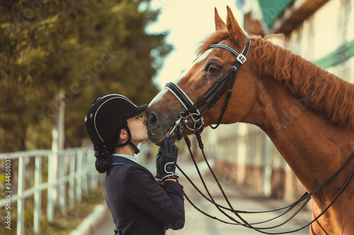 Young teenage girl equestrian kissing her favorite red horse. Multicolored outdoors horizontal image. Dressage outfit  © matilda553