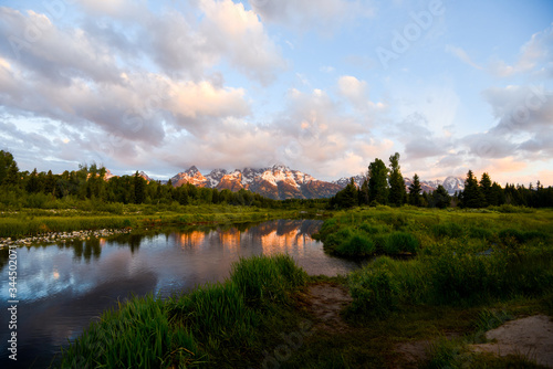 The early morning sun is illuminating the snow covered peaks of the  Grand Teon mountain range, reflecting in the still water of Snake River photo