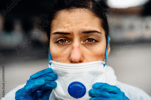 Exhausted doctor/nurse wearing coronavirus protective gear N95 mask uniform.Coronavirus Covid-19 outbreak.Mental stress of frontline worker.Face scars.Mask shortage.Overworked healthcare professional photo