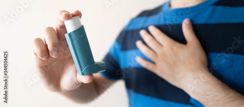 Young man using blue asthma inhaler for relief asthma attack. Pharmaceutical product is used to prevent and treat wheezing and shortness of breath caused asthma or COPD. Health care concept. Close up. photo