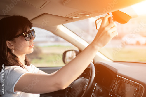 young caucasian woman inside a car in sunny day. Driver in sunglasses correct rearview mirror before start to drive. © Galina_lya