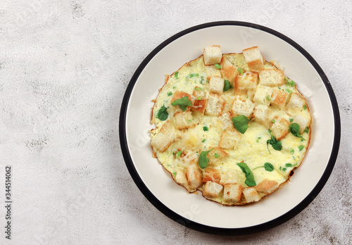 Omelette with sausages, green onions, cheese and croutons on a white round plate on a light gray background. Top view, flat lay