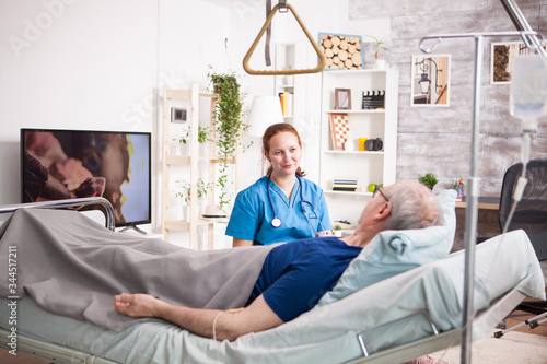 Sick old man laying on bed in nursing home and talking with female nurse. photo