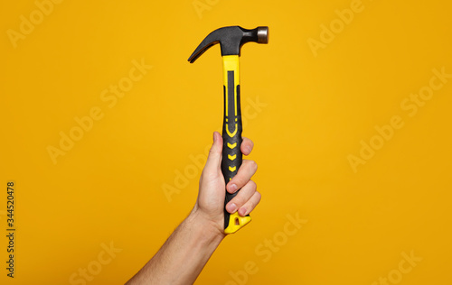 Carpenter hammer. Close-up photo of a hand holding a hammer on a yellow background. Home renovation concept.