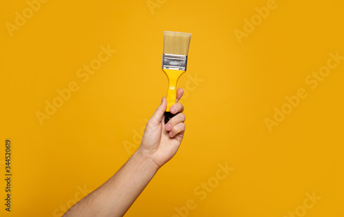 Paint brush. Close-up photo of a hand holding a paint brush on a yellow background. Home renovation concept.