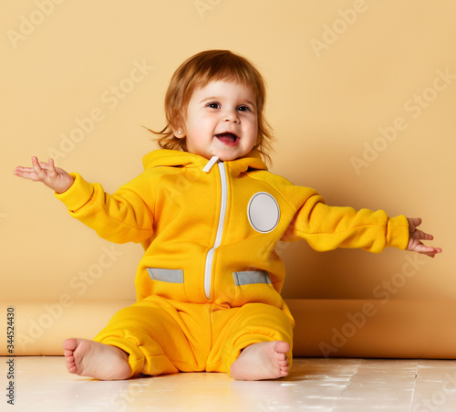 Infant child baby boy kid toddler in yellow body cloth sitting happy with hands raised up screaming 