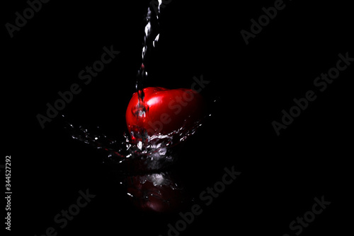 red tomato on a black background in water with splashes. fresh juicy red tomato