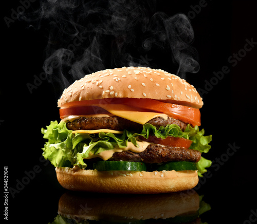 Double burger cheeseburger barbeque sandwich with beef  cheese and fresh vegetables hot with steam smoke on black