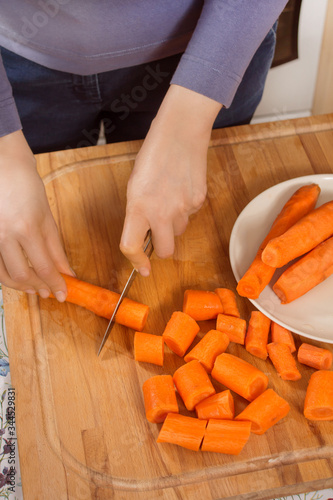 Kobieta kroi marchewki na desce kuchennej za pomocą noża. 