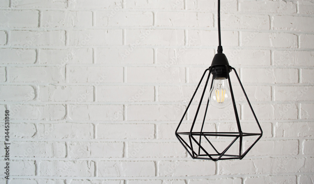 Modern black wire loft style chandelier against a white brick wall. Free space