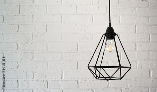 Modern black wire loft style chandelier against a white brick wall. Free space © Юлия