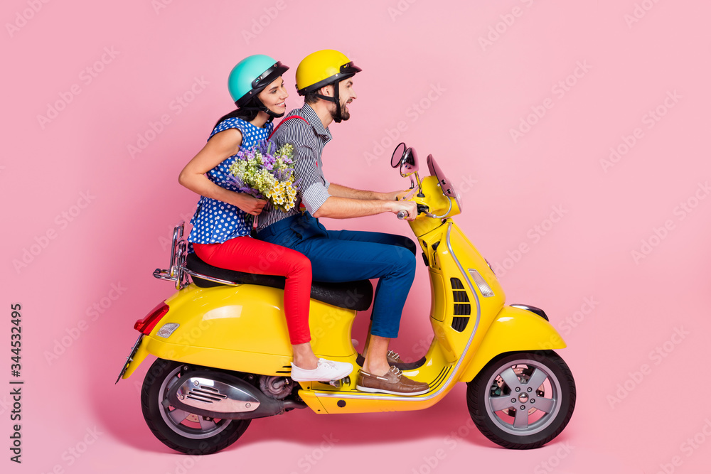 Full length profile side photo of positive cheerful bikers driver rider two people drive motor bike enjoy journey woman hold carry wildflowers bouquet isolated pastel color background Full length profile side photo of positive cheerful bikers driver rider two people drive motor bike enjoy journey woman hold carry wildflowers bouquet isolated pastel color background