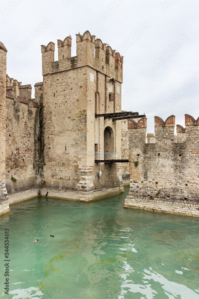 The water moat filled with water in front of the walls of the Castello Scaligero fortress, on Lake Garda in the Sirmione town in Lombardy, northern Italy