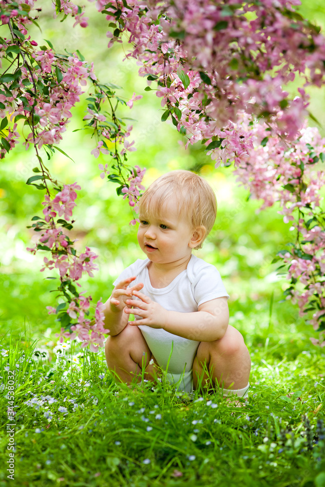 Close-up portrait of a 1-2 year old girl outdoors in a garden with pink flowers in the trees.