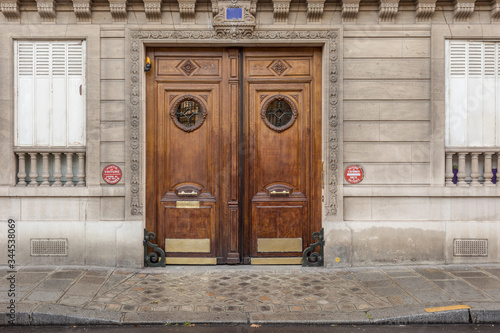 Two beautiful and decorative wooden doors on side of classic Paris building with wet sidewalk