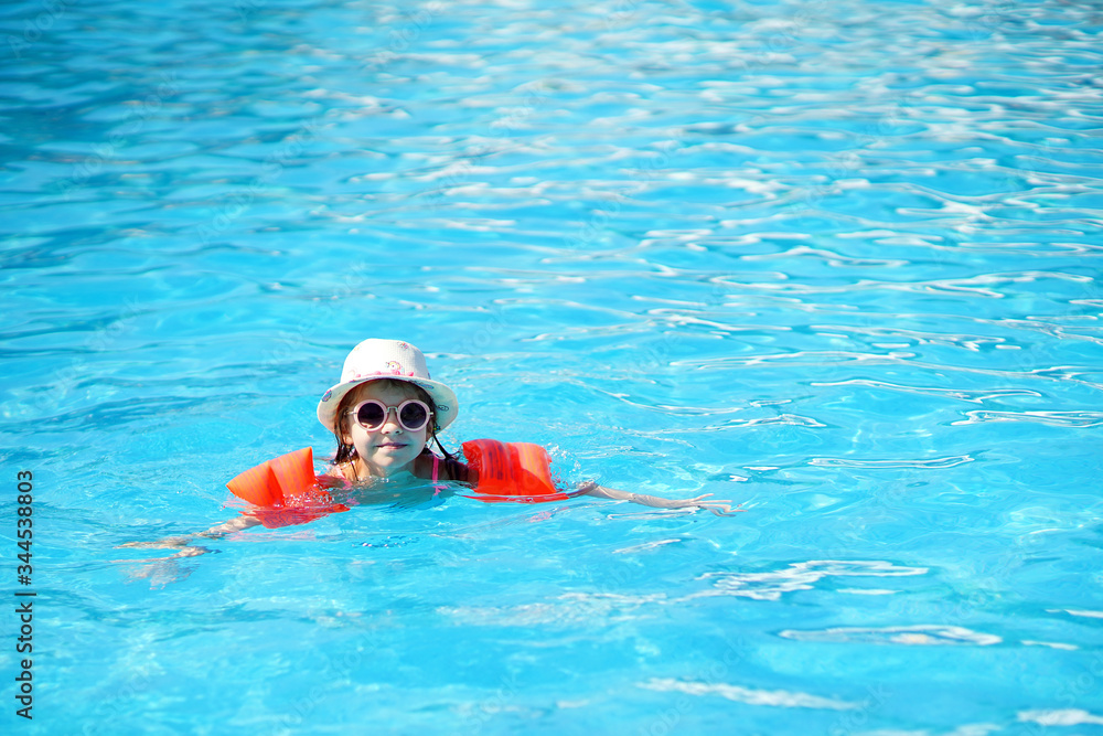 A charming child of European appearance, a girl 7-8 years old, swimming in the pool. Summer, a clear and sunny day. A girl with her family on vacation at sea. The girl has inflatable arm ruffles.