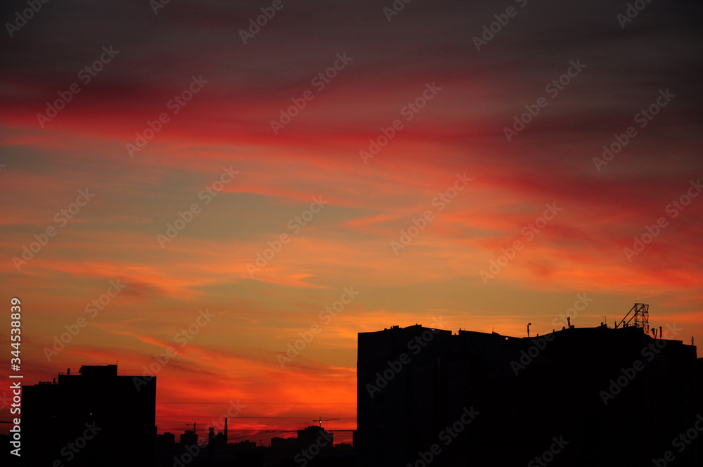 Urban landscape: beautiful sunset in the city with orange, red sky and black silhouettes of high residential apartment buildings.