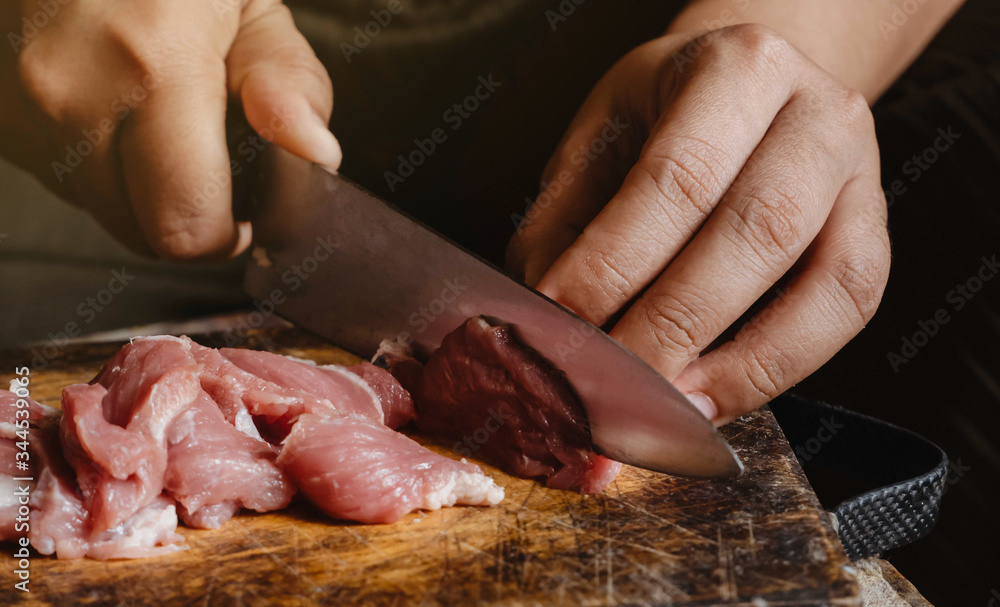 The hand of a young woman slicing pork into small pieces in order to cook different types of food, home cooking. Concept
