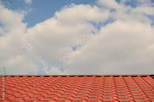 Red roof of a house on a blue sky with clouds