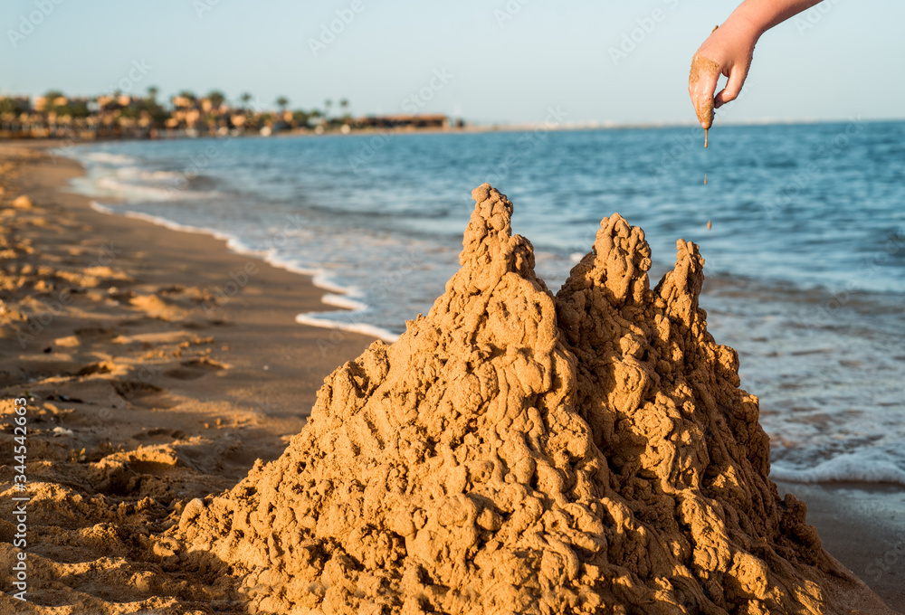 Sand castle made of sand by the hands of a child on the shore.Sea at sunset, white sand on the beach.Sunset sun, yellow light.Empty beach, nobody. Without people