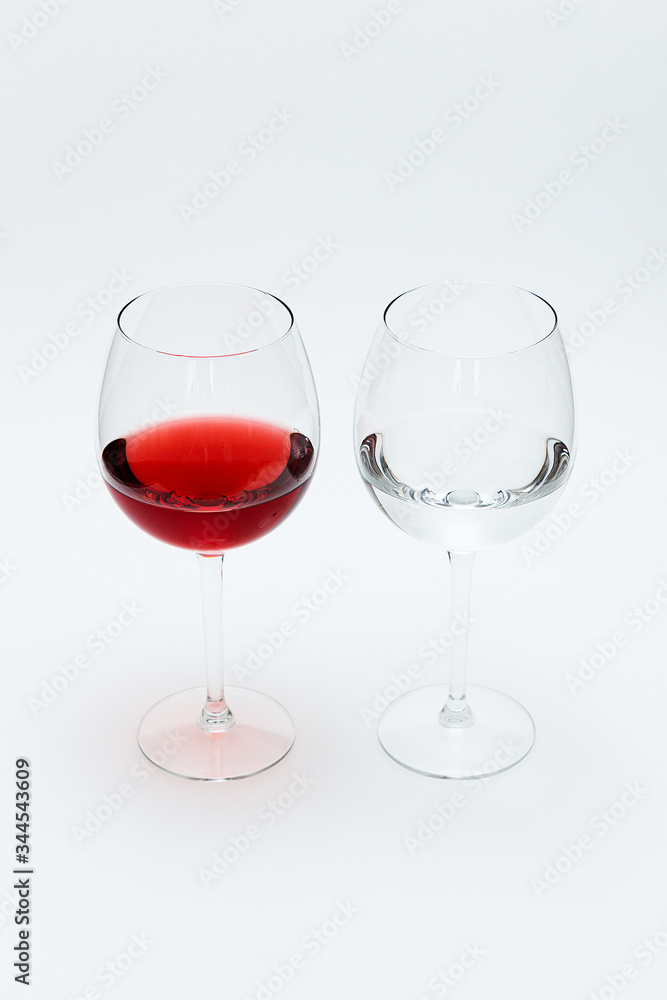 Two glasses on a white table. One is filled with red wine, the other is water.