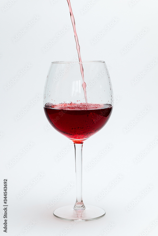 Red wine is poured into a large glass on a white background Red wine is poured into a large glass on a white background
