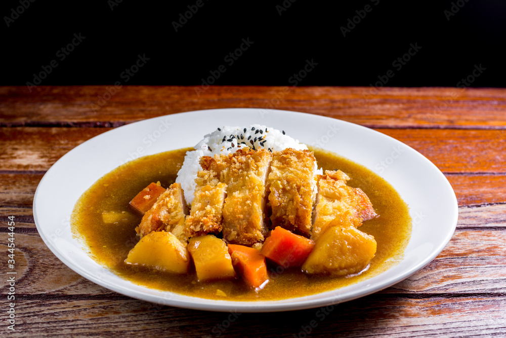 Japanese curry with rice, black sesame, carrot, potato and deep fries chicken in white dish on wooden table. Japanese curry with rice, black sesame, carrot, potato and deep fries chicken in white dish on wooden table.