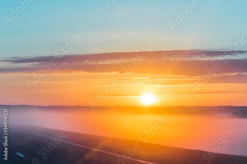 Dawn with fog, foggy road. Beautiful landscape early in the morning with bright orange rising sun and clouds
