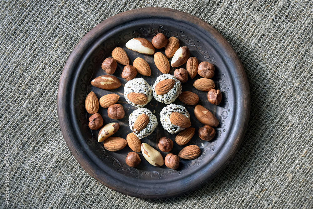 Obraz premium Various nuts are laid out in a brown handmade clay plate placed on a gray burlap.