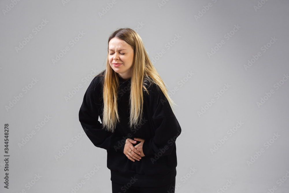 Young caucasian woman suffers from abdominal pain, feels sick, ill and weakness isolted on gray studio background. Symptoms of desease or unhealthy lifestyle. Sickness, ilness, sad and upset Young caucasian woman suffers from abdominal pain, feels sick, ill and weakness isolted on gray studio background. Symptoms of desease or unhealthy lifestyle. Sickness, ilness, sad and upset